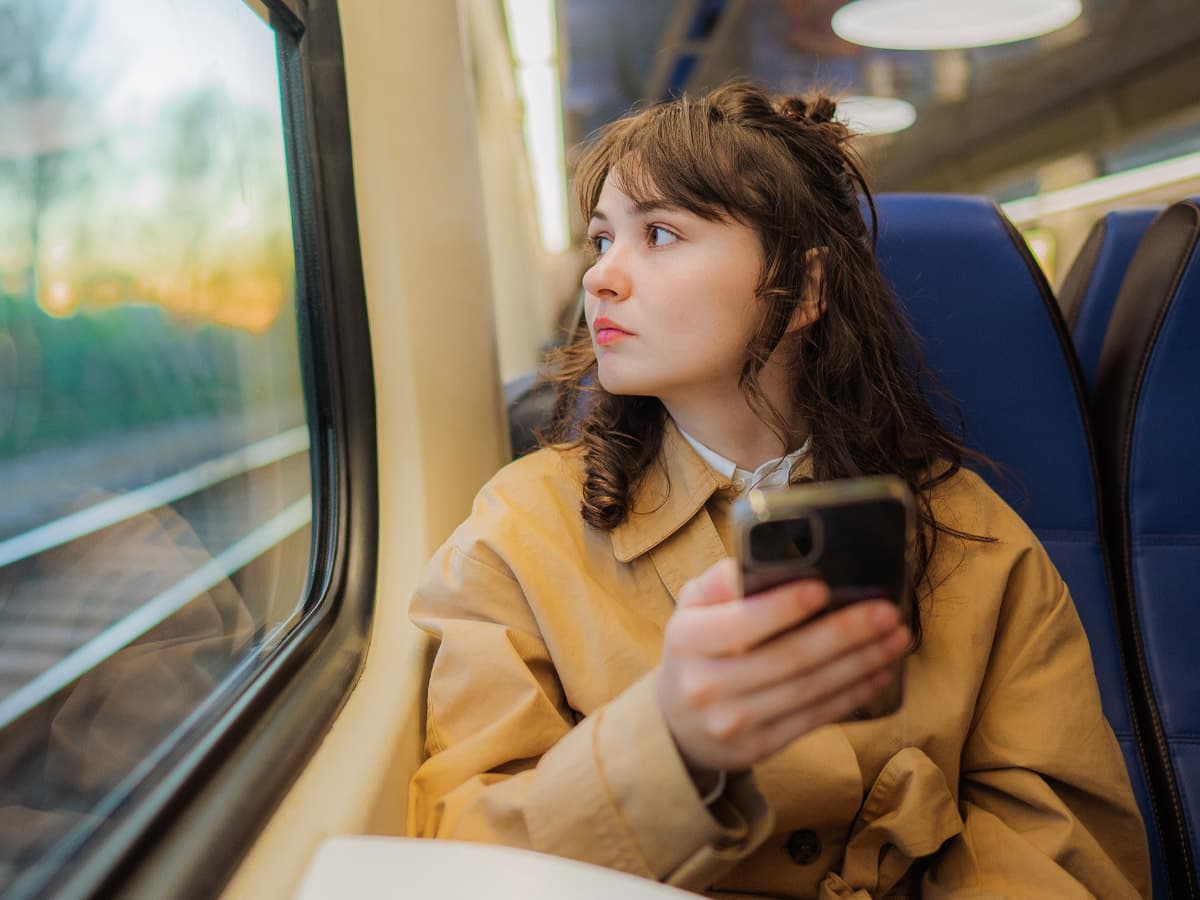 A woman looks out the train window, observing the passing landscape with a contemplative expression