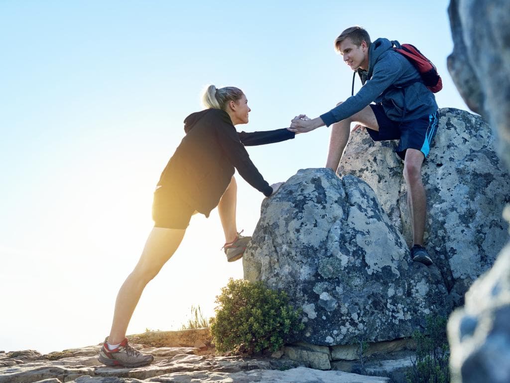 En mand og en kvinde hjælper hinanden, mens de bestiger et bjerg, og viser teamwork og beslutsomhed i et barskt landskab