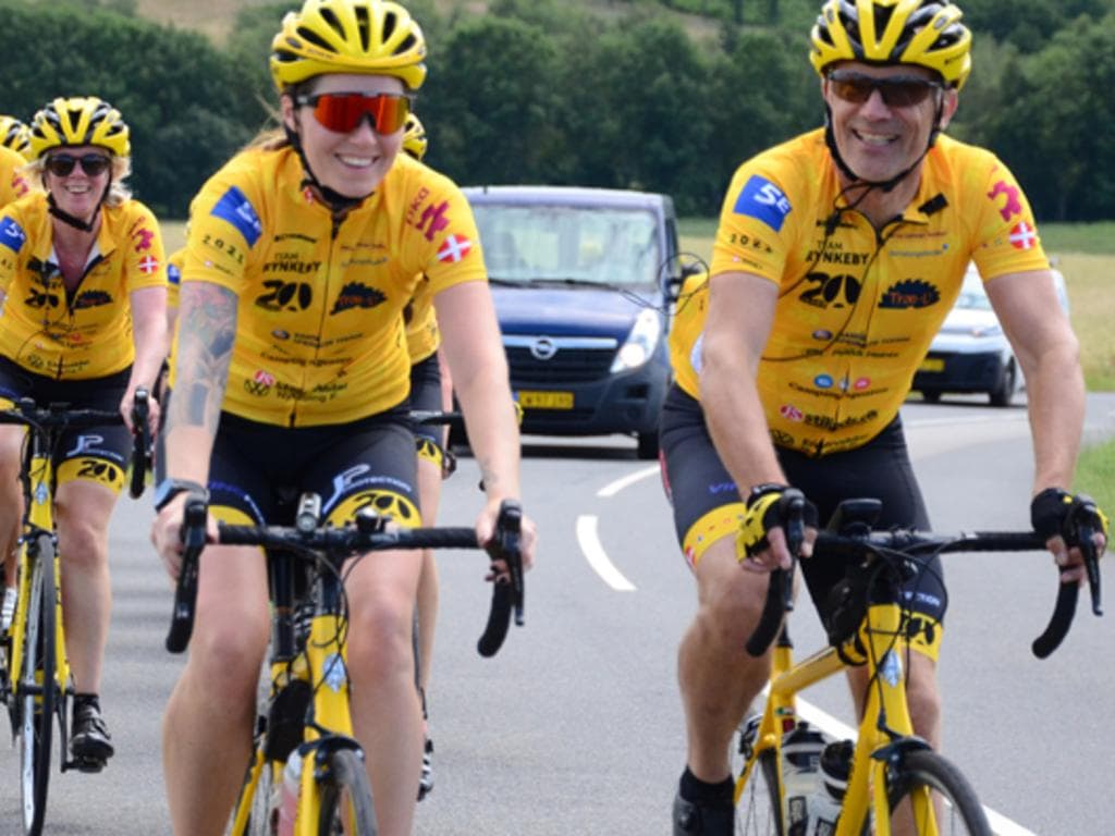 En gruppe cyklister iført gule trøjer og hjelme kører sammen på en solrig dag